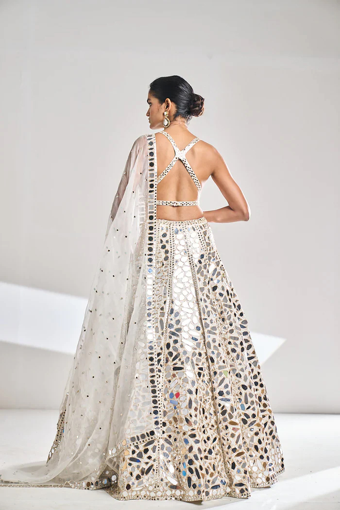 A woman stands with her back to the camera in a sleeveless, floor-length gown with a mosaic pattern and mirrored embellishments.