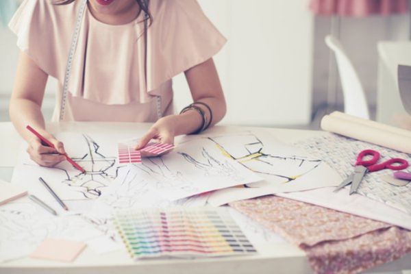 A person is sitting at a table, sketching fashion designs.