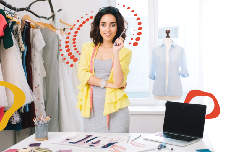 A woman in a yellow blazer and gray dress stands in a fashion studio with a pencil, laptop, sketches, fabric swatches, and a mannequin.